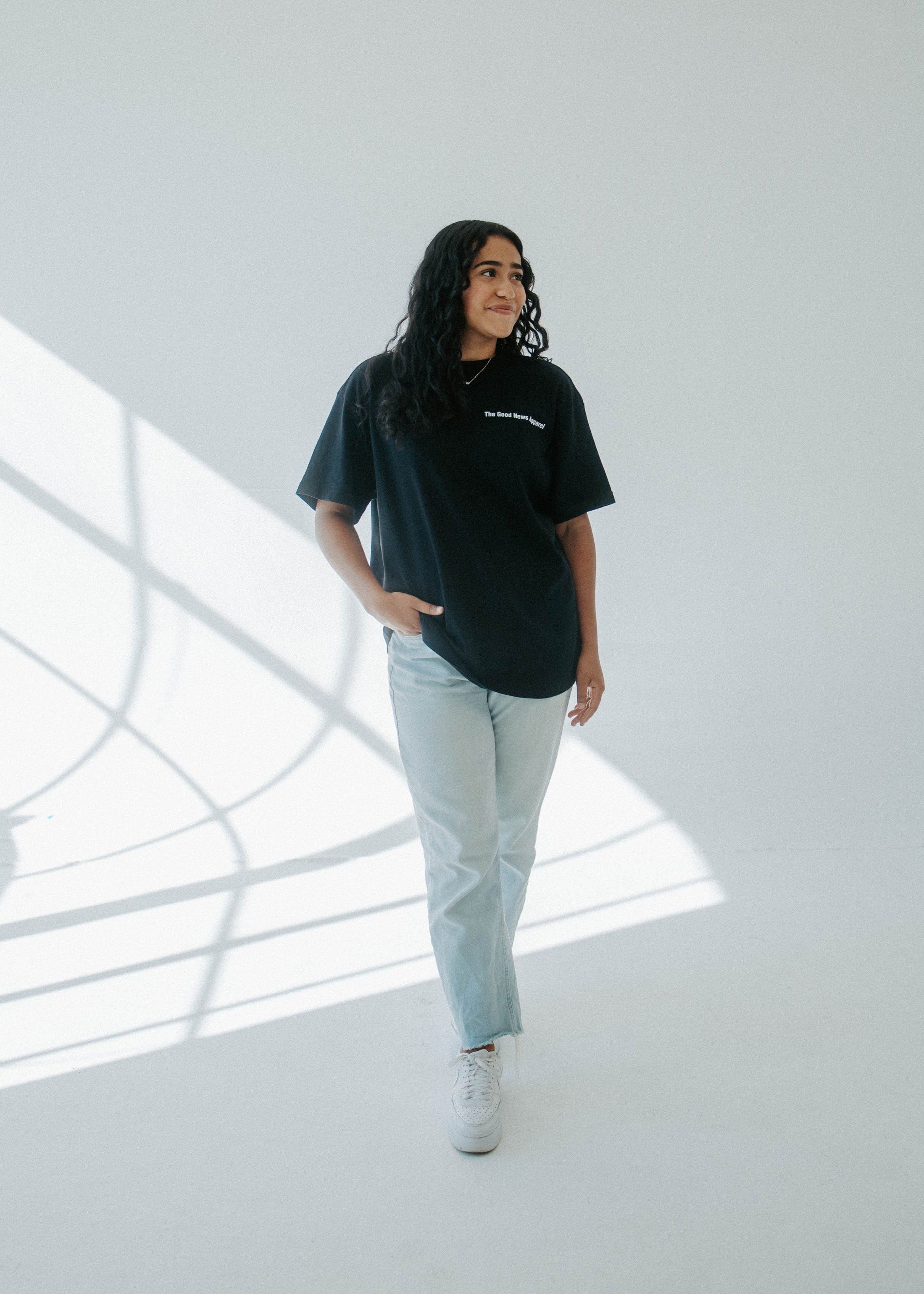 Person wearing a black t-shirt and light blue jeans standing in a modern indoor setting with large windows.