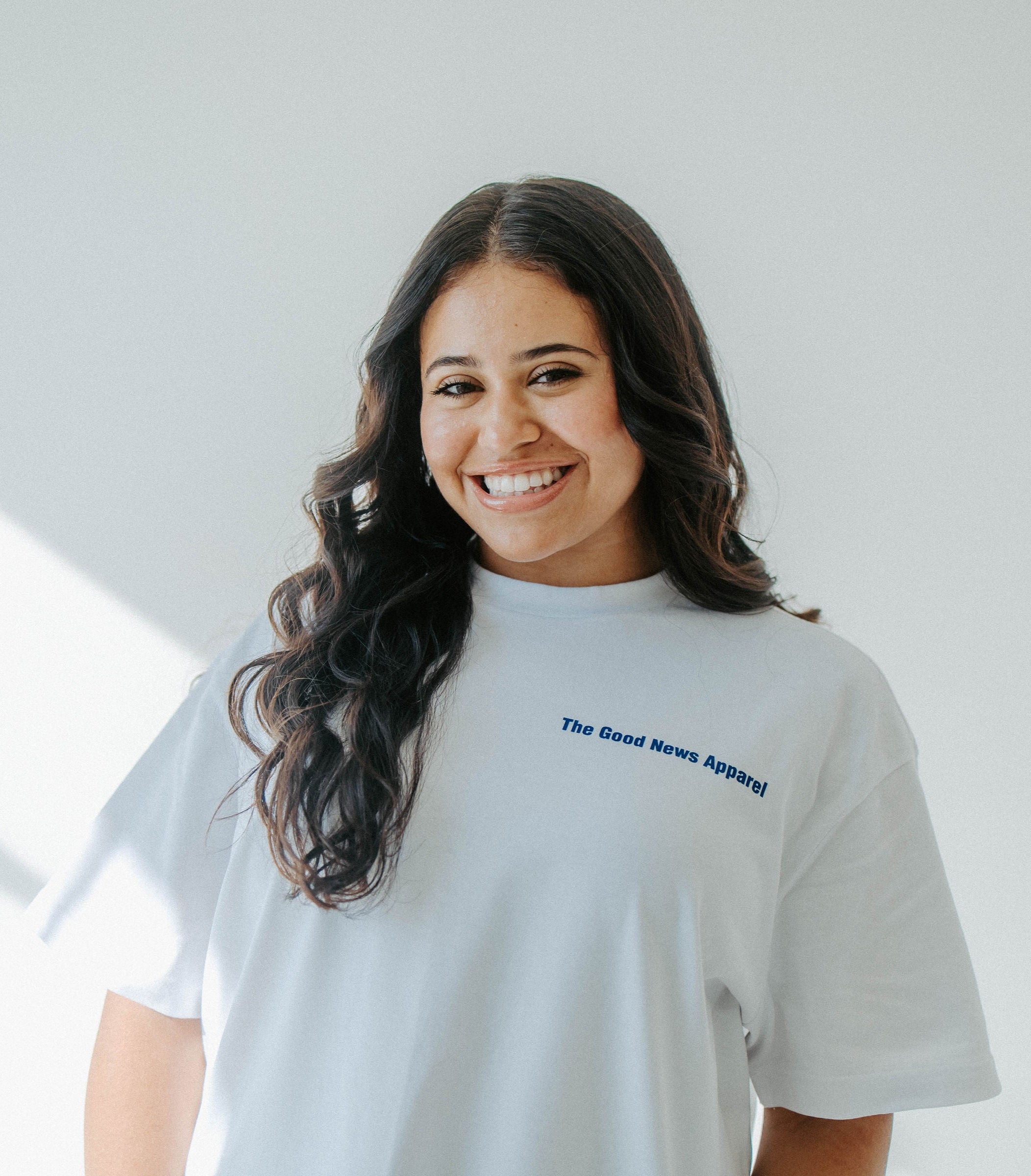 Woman wearing a light gray t-shirt with text, standing in a bright room.