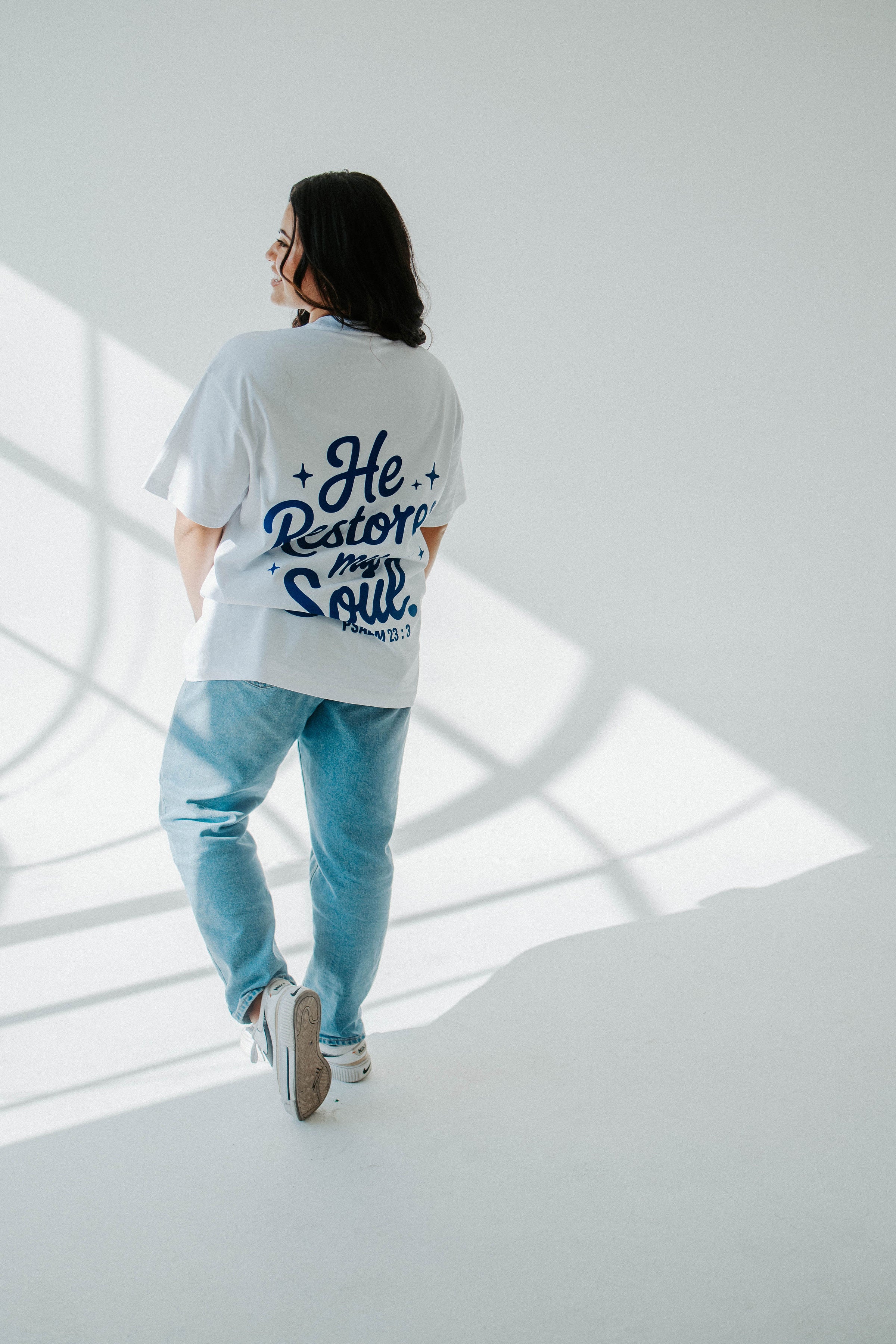 Person wearing a white t-shirt with text and light blue jeans in a modern architectural setting