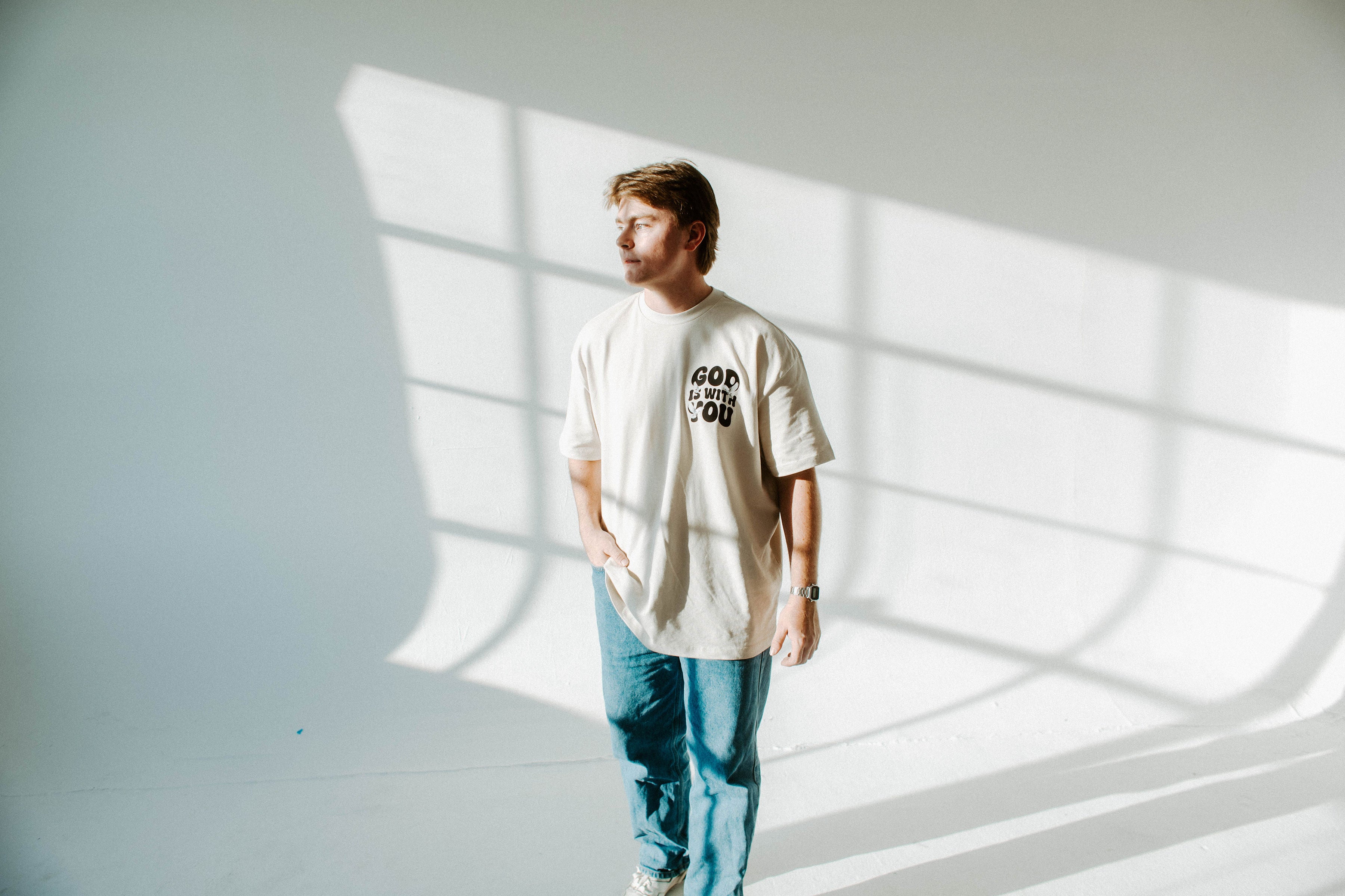 Person wearing a beige t-shirt with text standing in a room with light patterns on the wall