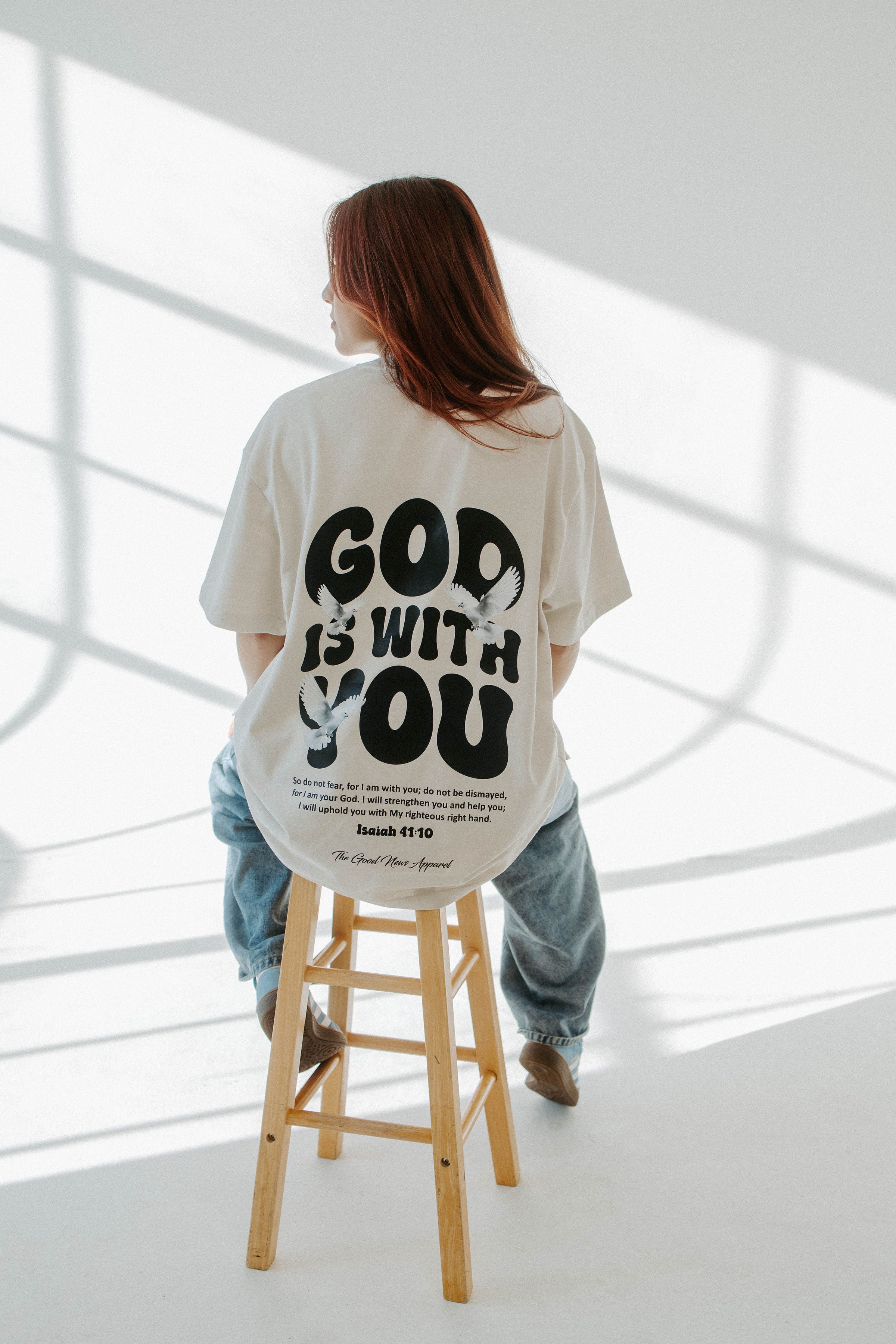 Person wearing a white t-shirt with 'GOD IS WITH YOU' text in a minimalistic setting