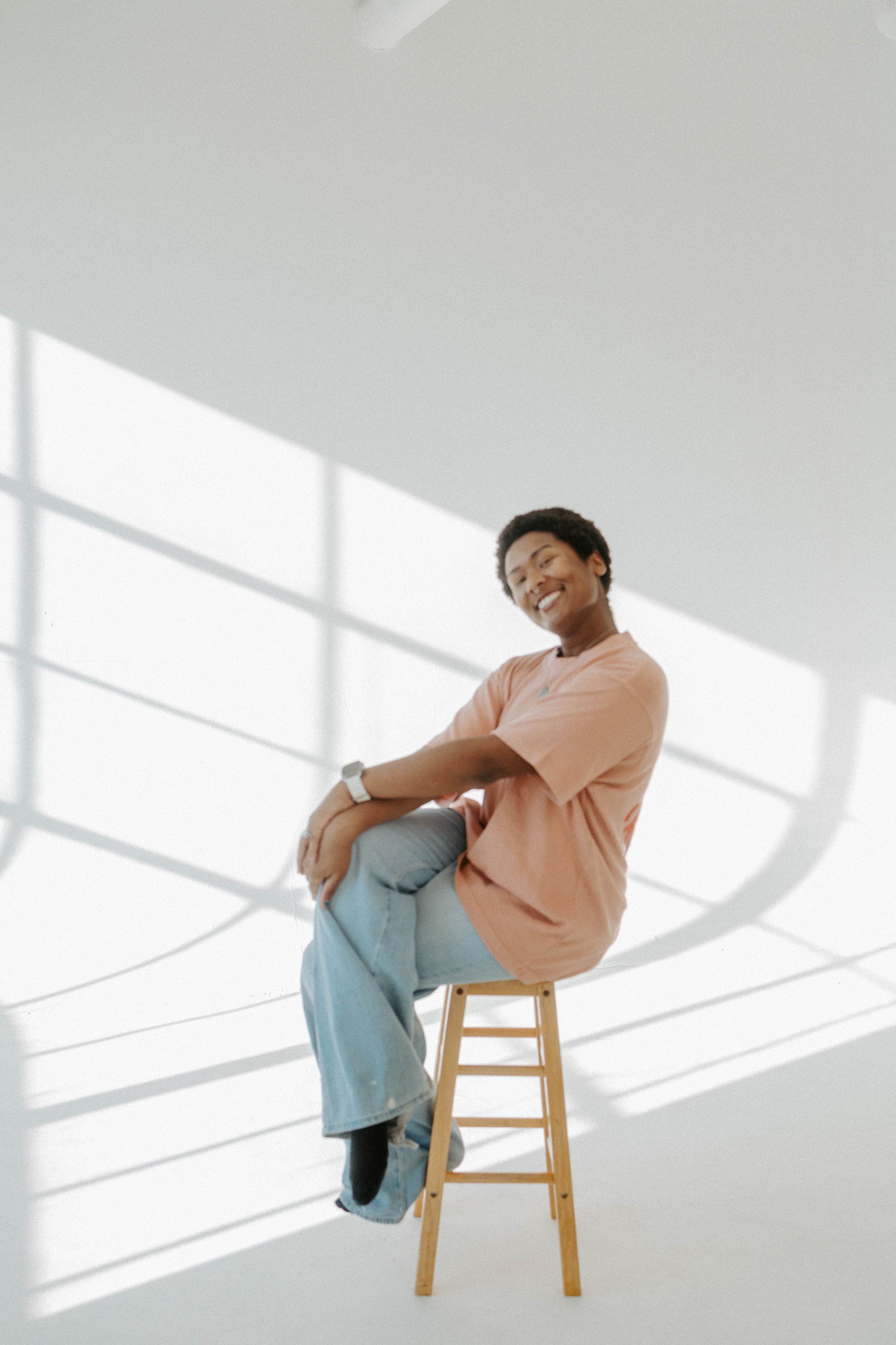 Person sitting on a stool in a bright, modern room with large windows.