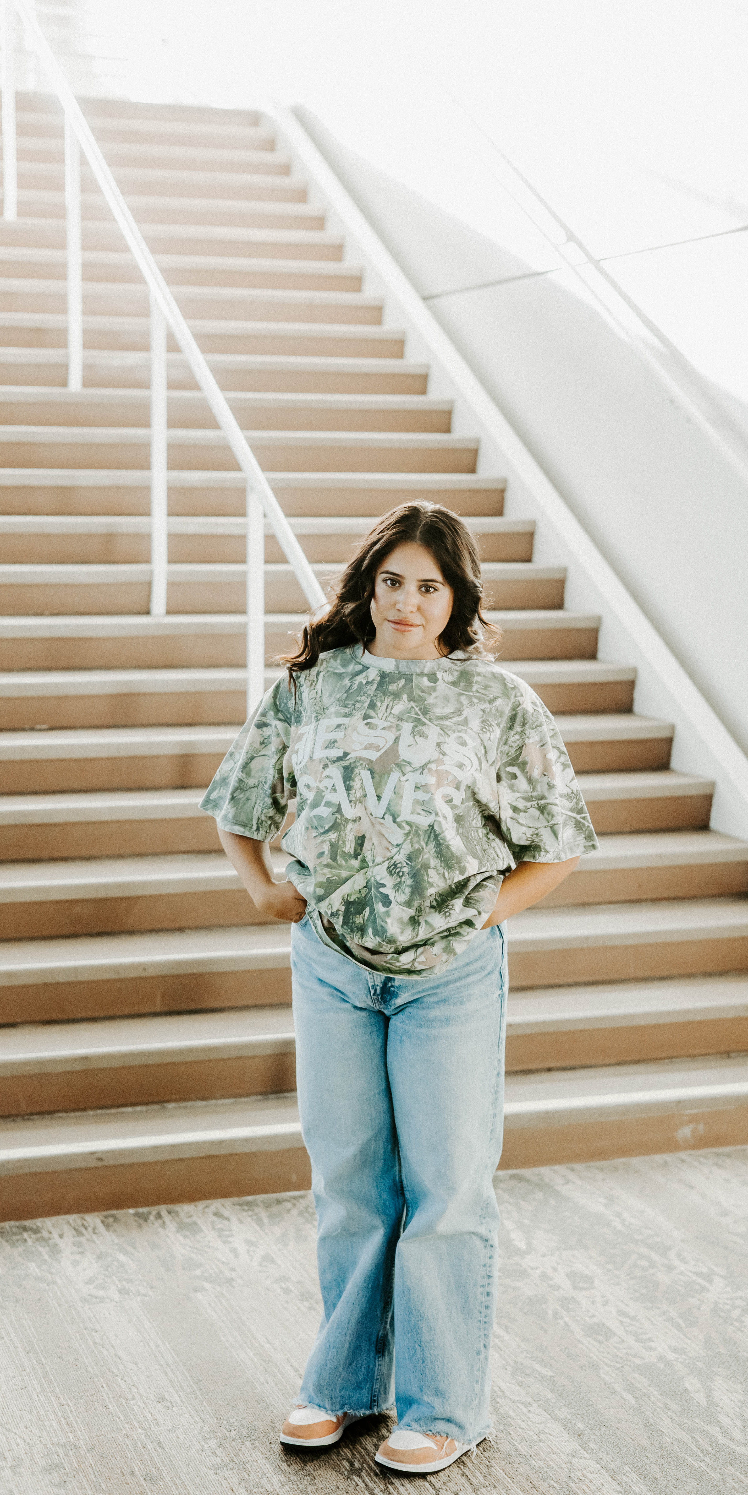 Woman standing on a staircase wearing a floral top and jeans.