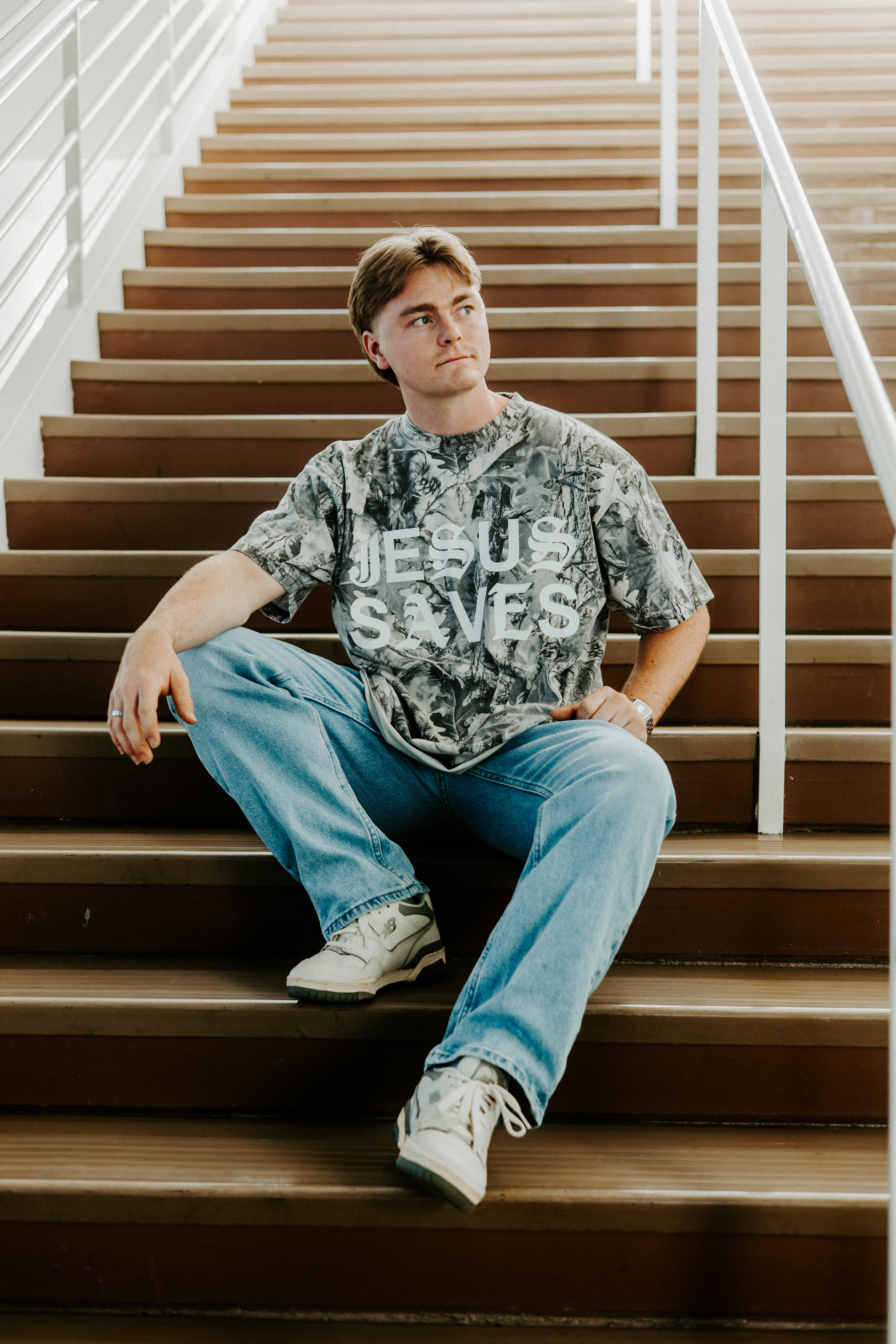 Person sitting on a staircase wearing a t-shirt with 'Jesus Saves' text.
