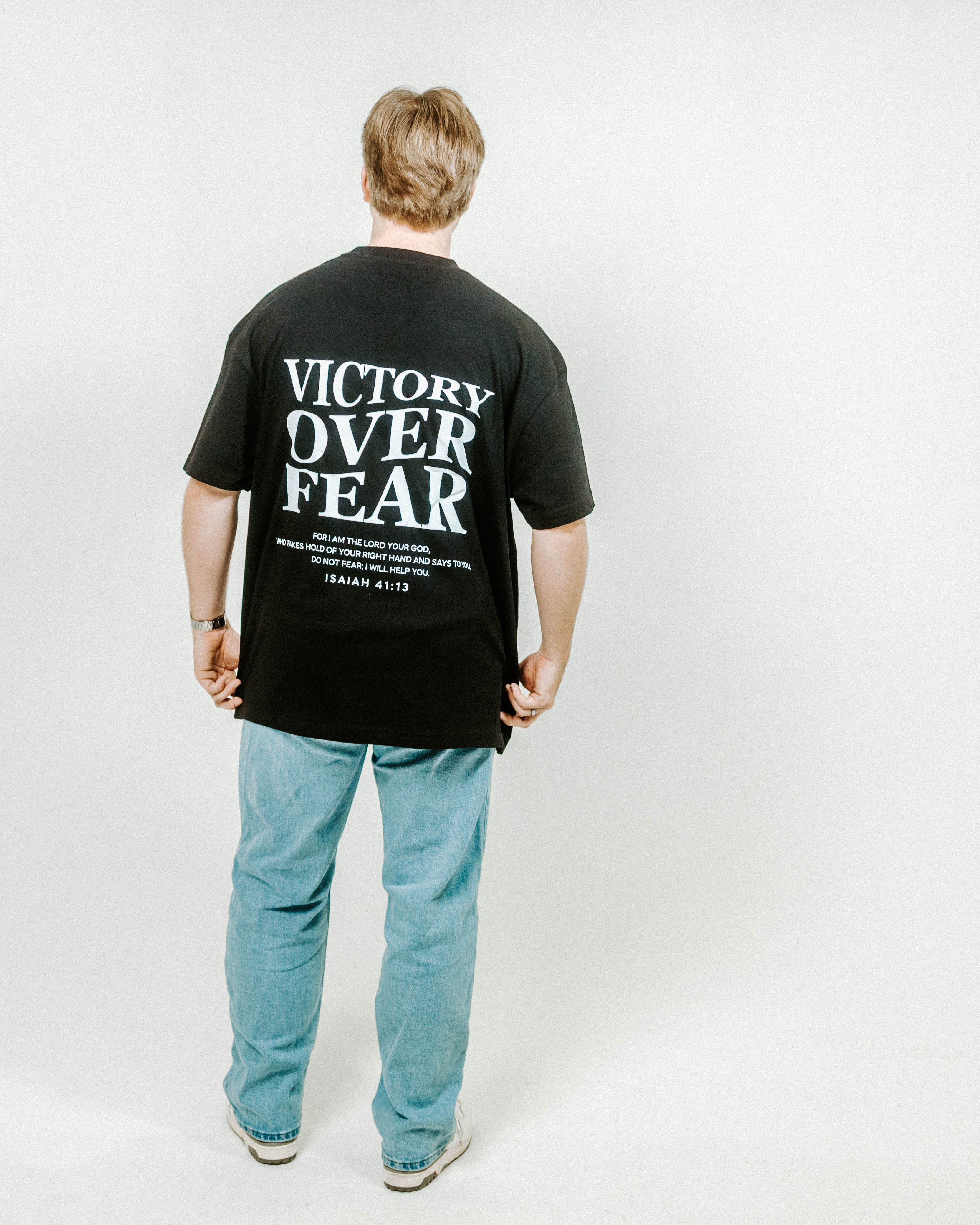 Person wearing a black t-shirt with 'Victory Over Fear' text on the back, standing against a white background