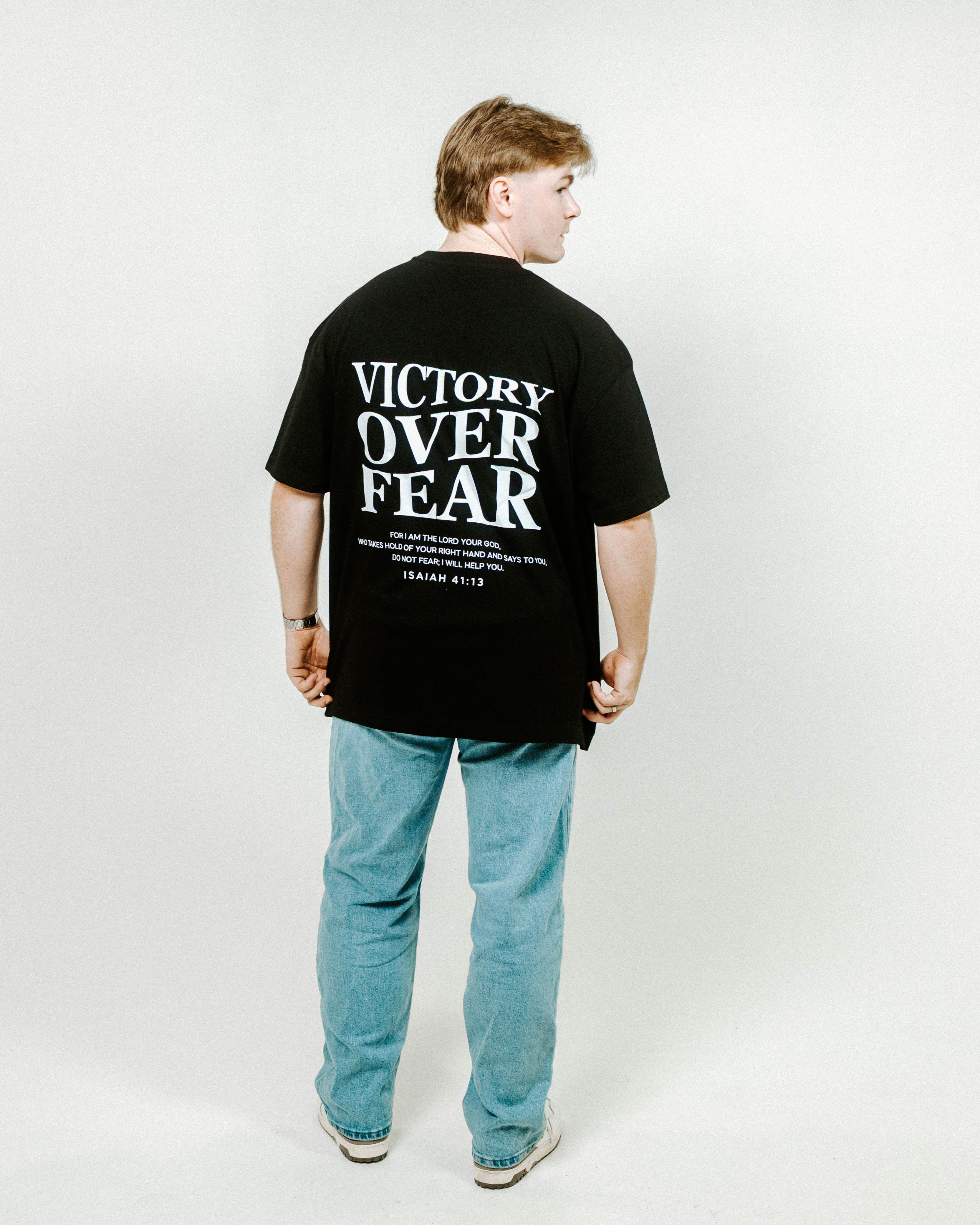 Person wearing a black t-shirt with 'Victory Over Fear' text on the back, standing against a white background