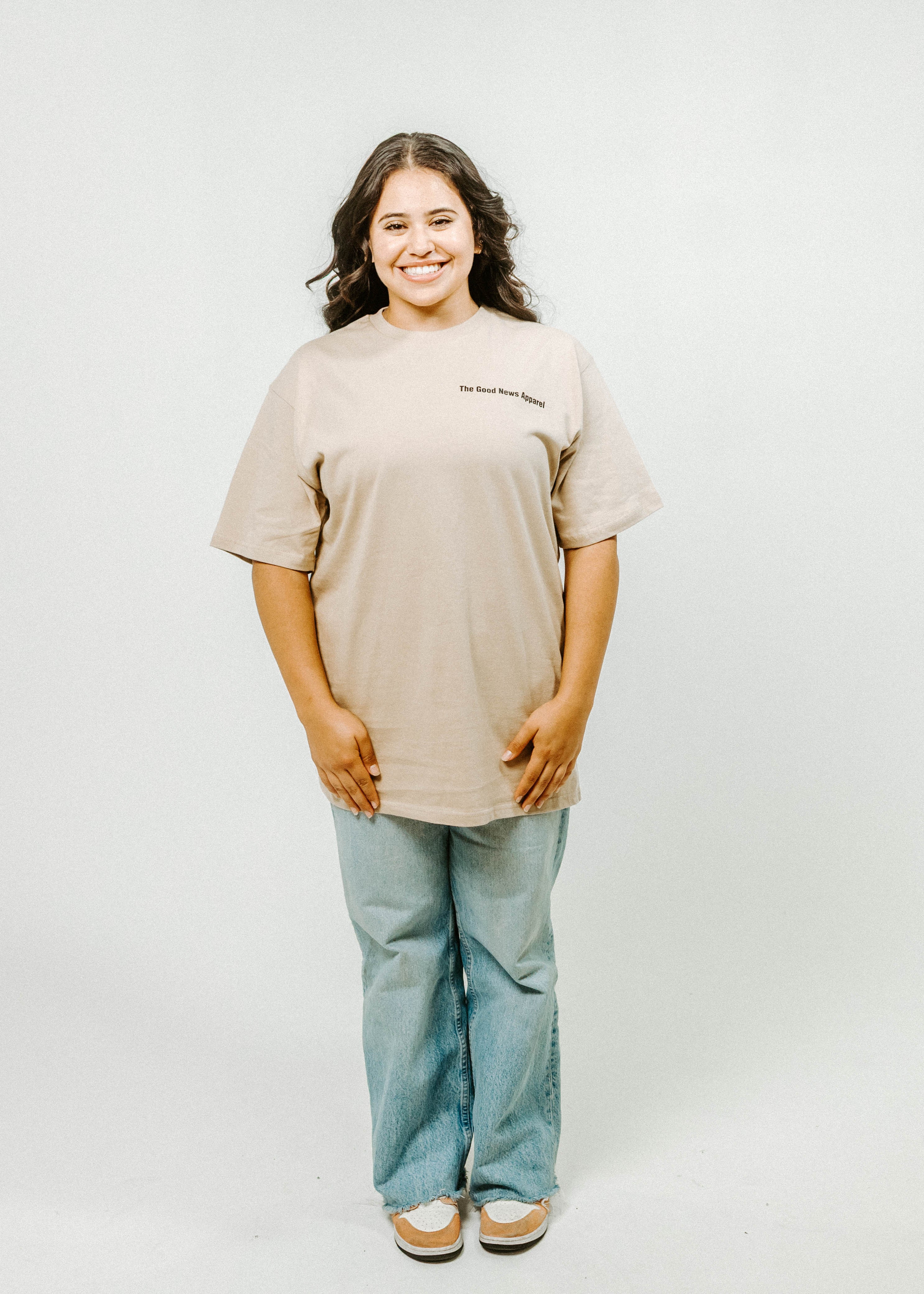 Person wearing a beige t-shirt and light blue jeans on a white background