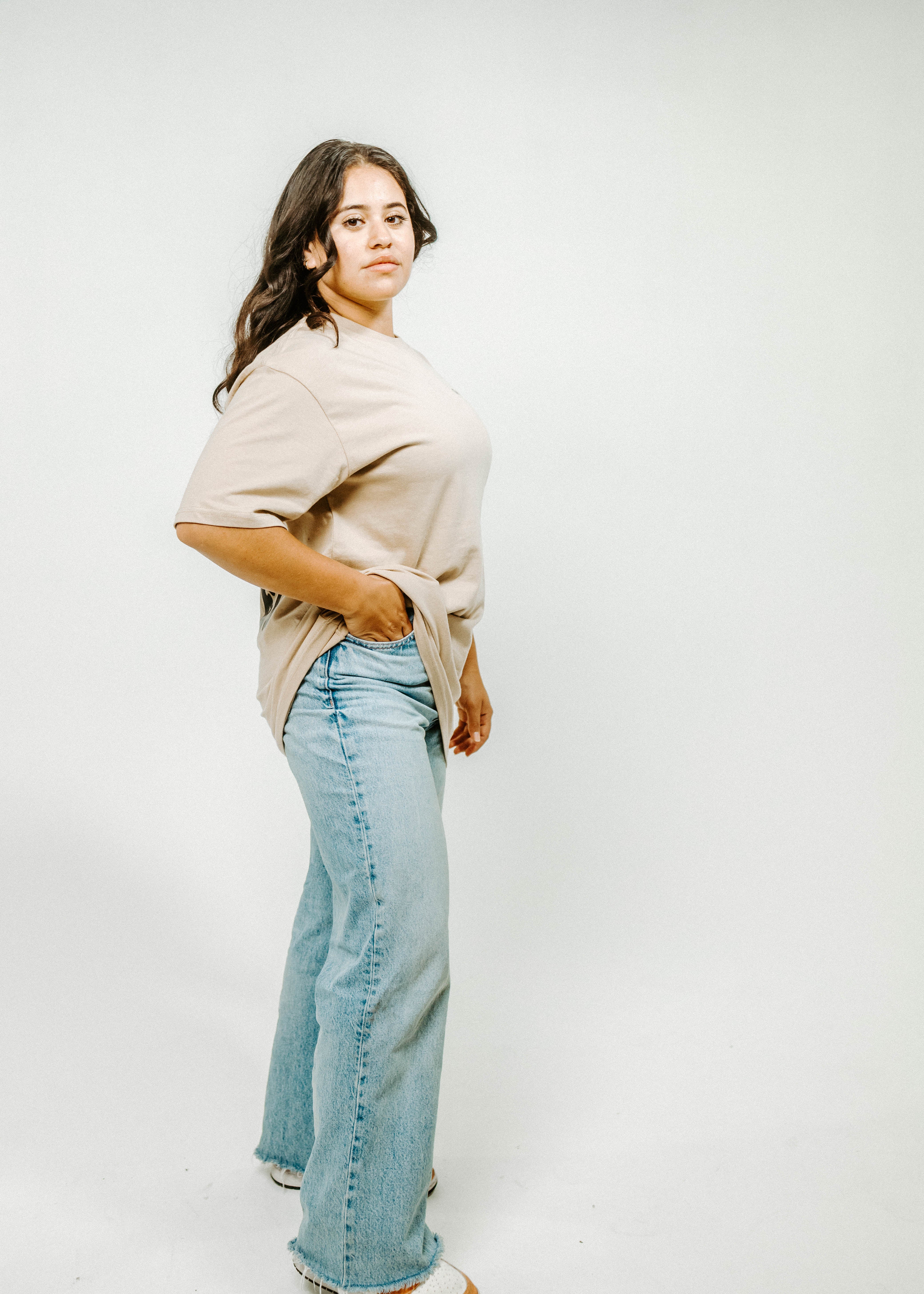 Woman wearing a beige sweater and light blue jeans against a white background