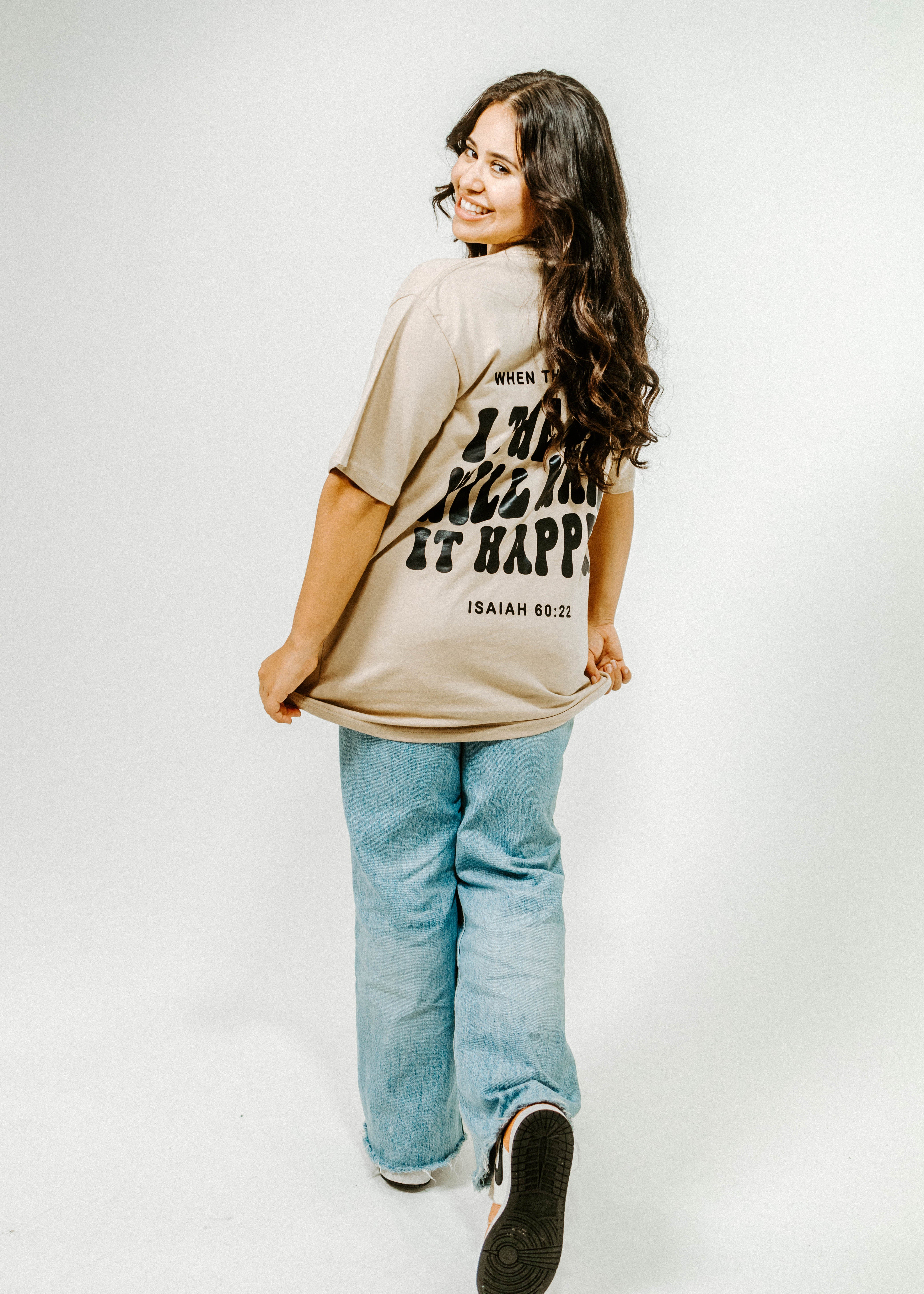 Person wearing a beige t-shirt with text and light blue jeans on a white background