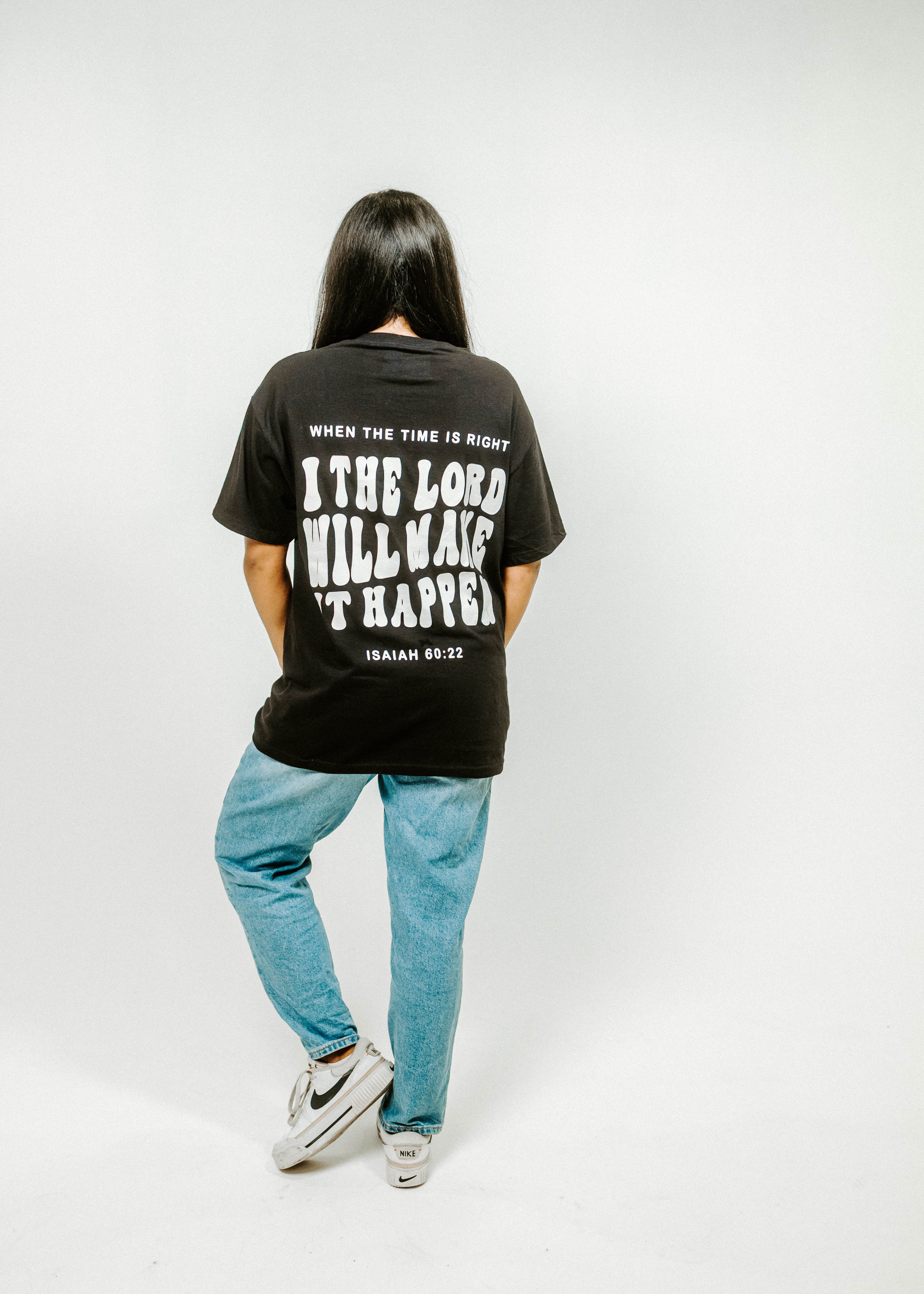 Person wearing a black t-shirt with text on the back, standing against a white background