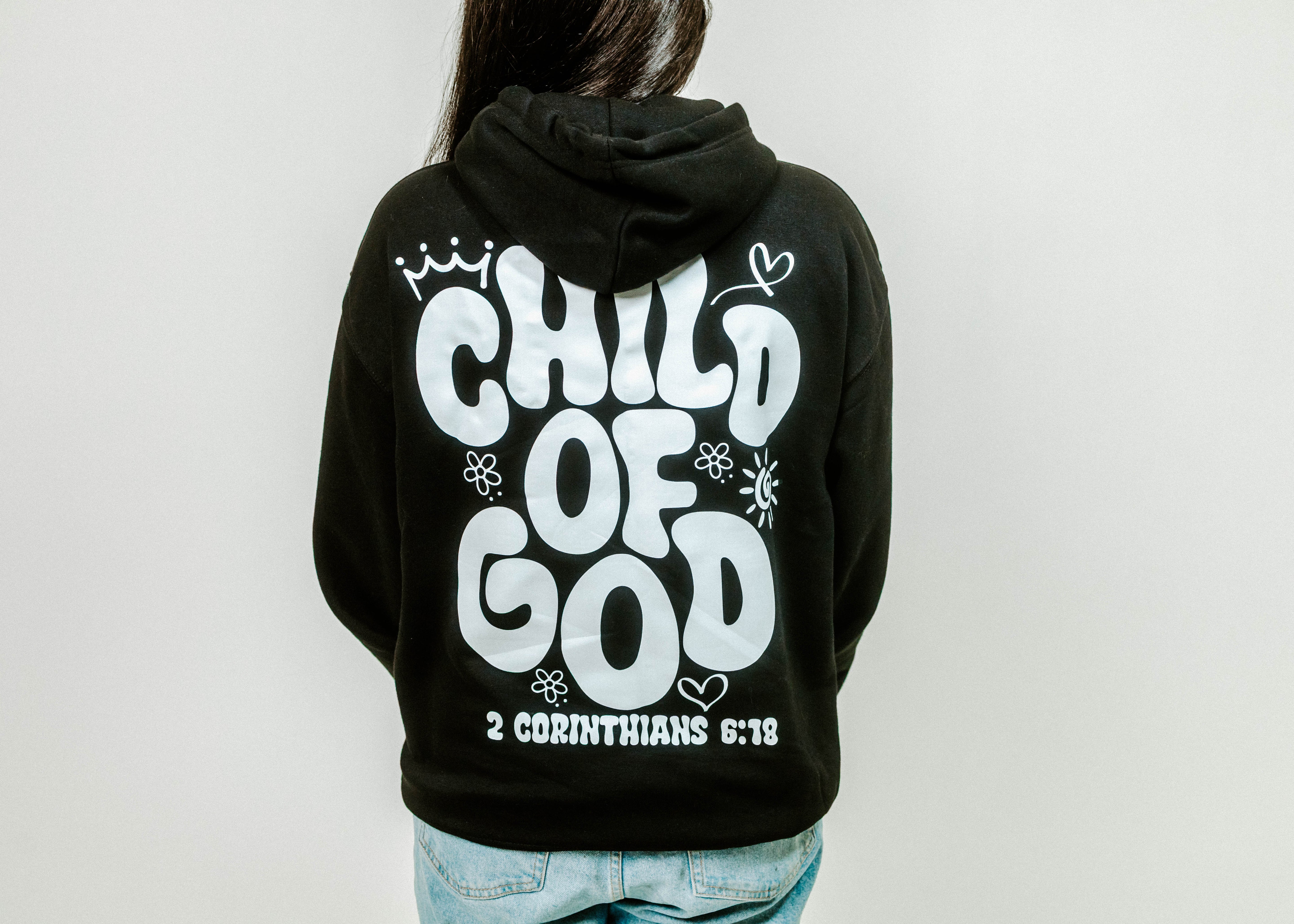 Black hoodie with 'Child of God' text on the back, worn by a person against a plain background