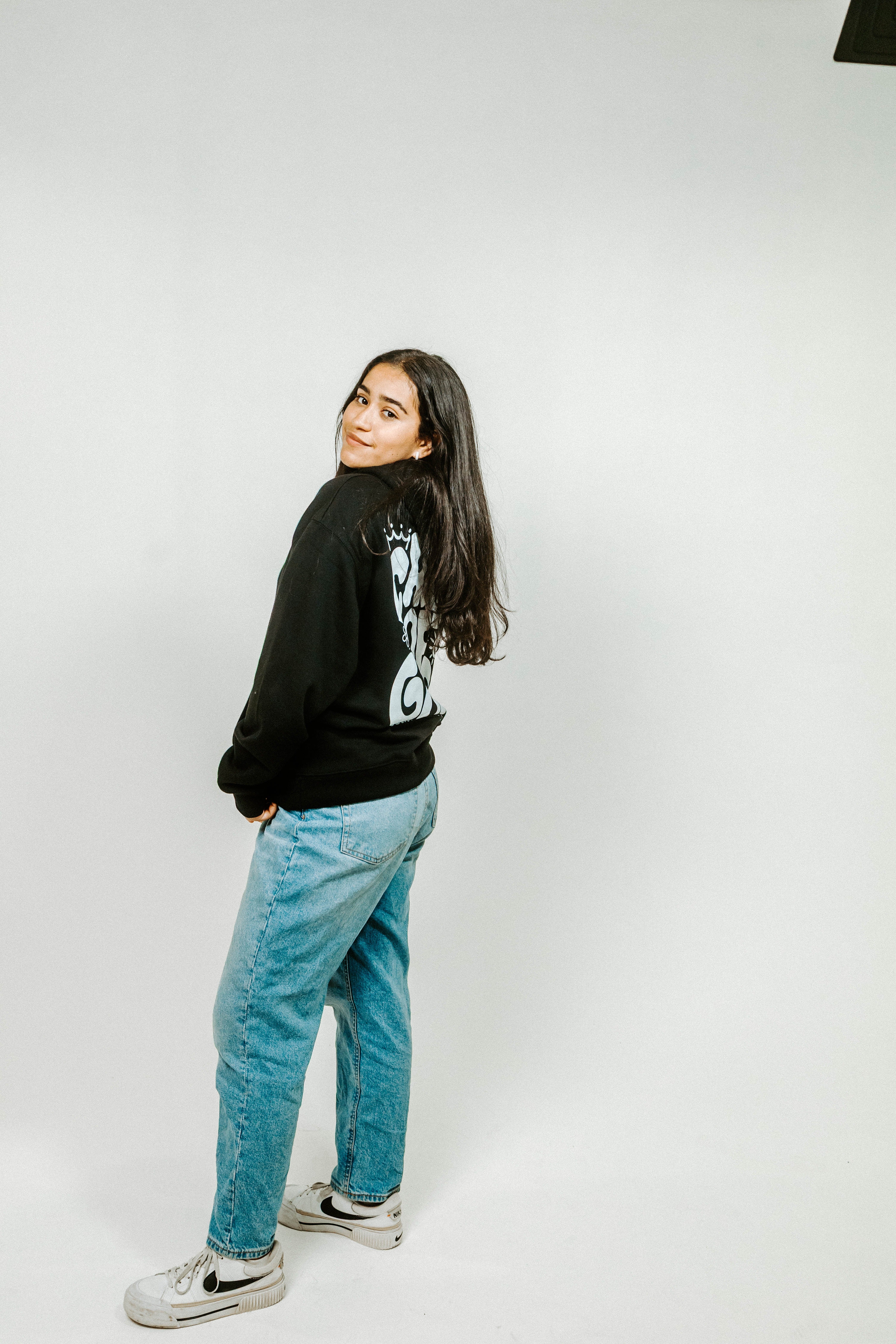 Person wearing a black sweatshirt with a graphic design and blue jeans on a white background