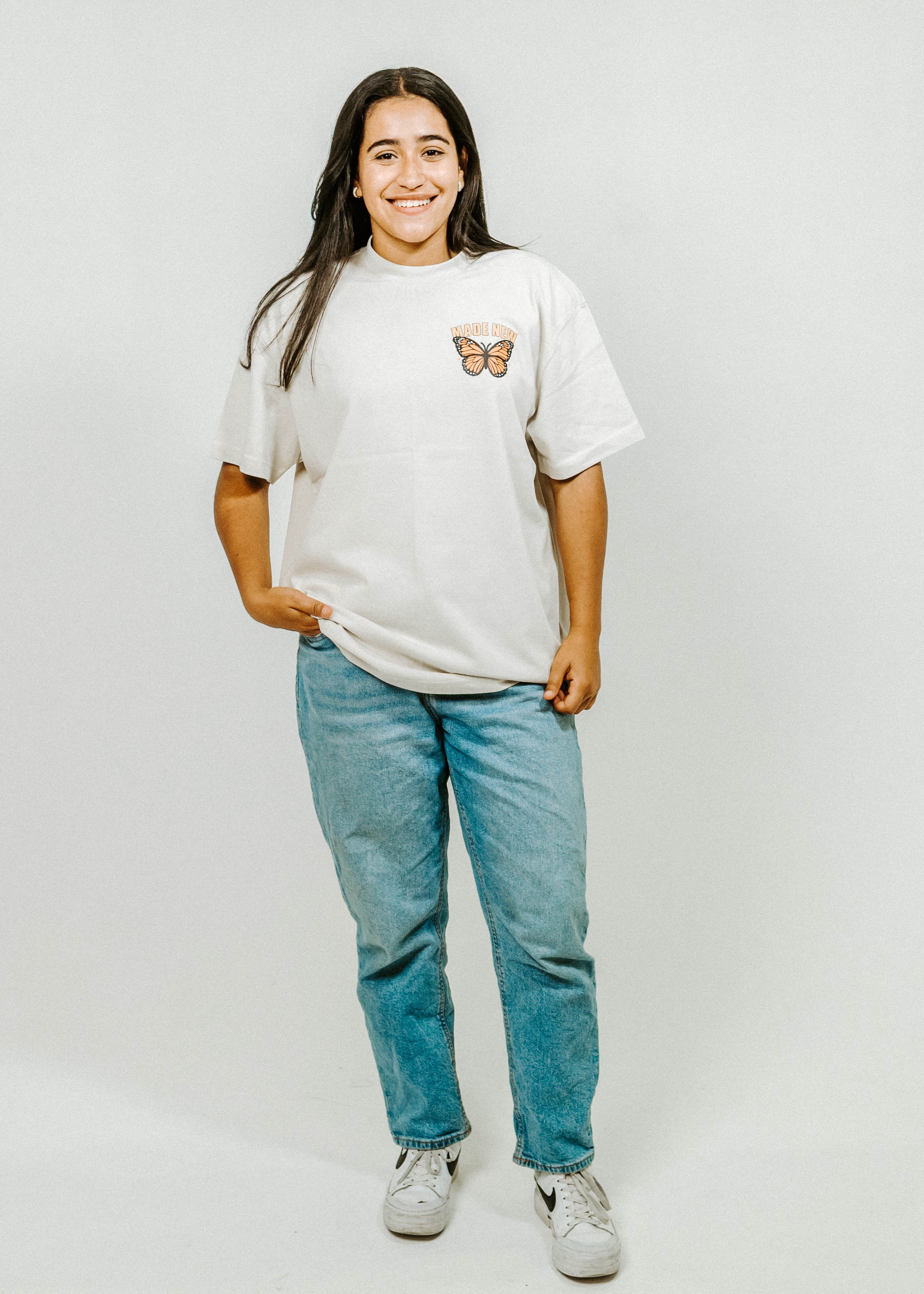 Person wearing a white t-shirt with a butterfly design and blue jeans on a plain background