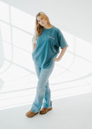 Woman wearing a blue oversized shirt and jeans standing in a bright, minimalistic room.
