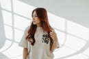 Woman wearing a white t-shirt with text, standing in a room with light filtering through.