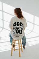 Person wearing a white t-shirt with 'GOD IS WITH YOU' text in a minimalistic setting