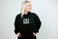 Person wearing a black hoodie with a white emblem on a plain background