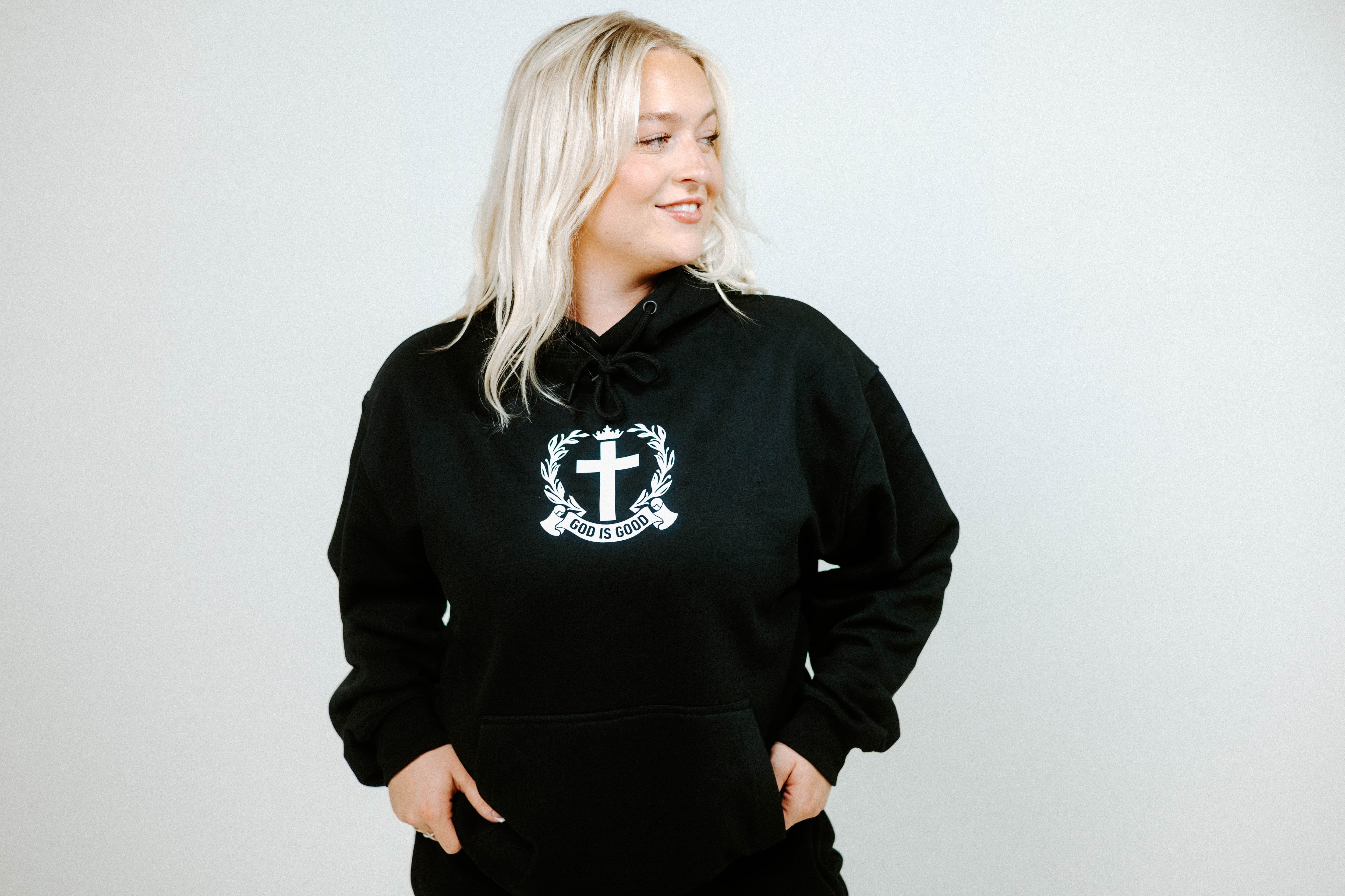 Person wearing a black hoodie with a white emblem on a plain background