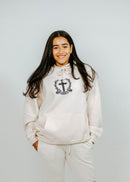 Person wearing a white hoodie and pants with logos on a plain background