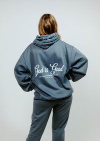 Person wearing a gray hoodie with 'God is Good' text on the back against a white background