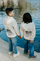 A child standing outdoors wearing a soft beige hoodie with the faith message “Created With a Purpose” printed on the back