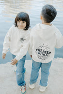 Child wearing a cream Christian kids hoodie with “Created With a Purpose” on the back.