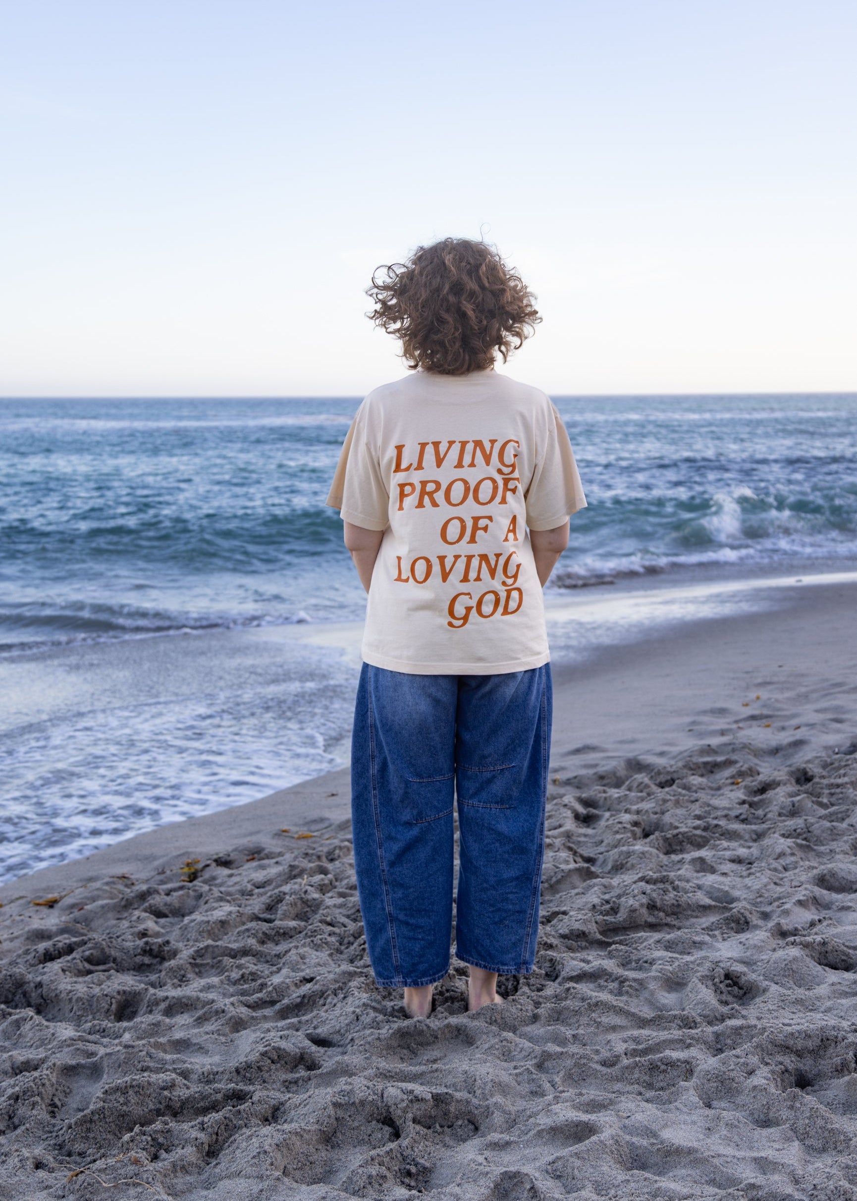 Woman wearing the Living Proof of a Loving God oversized Christian graphic tee in cream.