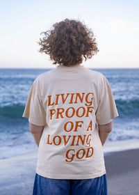 Woman wearing the Living Proof of a Loving God oversized Christian graphic tee in cream.