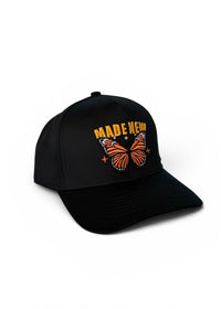 Black cap with orange butterfly design and 'MADE HERE' text on a white background