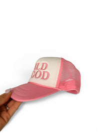 Pink and white cap with 'Wild God' text held by a hand on a white background