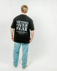 Person wearing a black t-shirt with 'Victory Over Fear' text on the back, standing against a white background