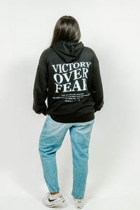 Person wearing a black hoodie with 'Victory Over Fear' text on the back, standing against a white background.