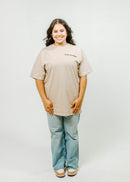 Person wearing a beige t-shirt and light blue jeans on a white background