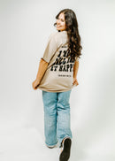 Person wearing a beige t-shirt with text and light blue jeans on a white background