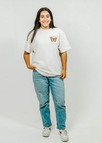 Person wearing a white t-shirt with a butterfly design and blue jeans on a plain background