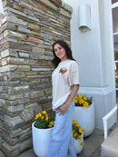 Woman standing outdoors next to a stone wall with potted yellow flowers.