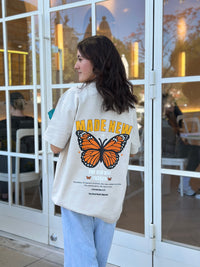 Person wearing a white sweatshirt with a butterfly graphic and 'MADE NEW' text in an indoor setting.
