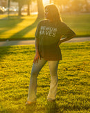 Person wearing a shirt with text standing in a park at sunset