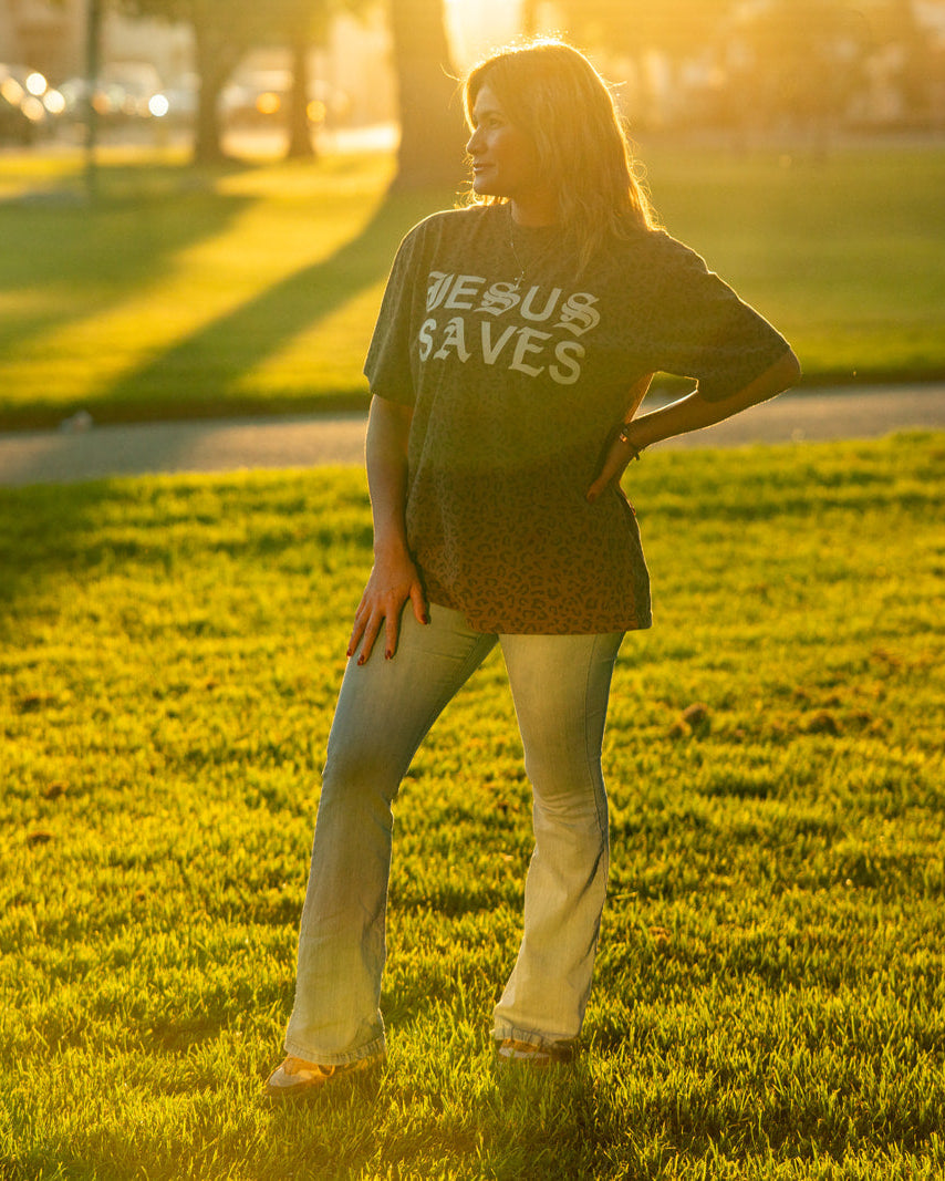 Person wearing a shirt with text standing in a park at sunset