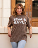 Woman wearing a brown t-shirt with 'Jesus Saves' text, standing against a building.