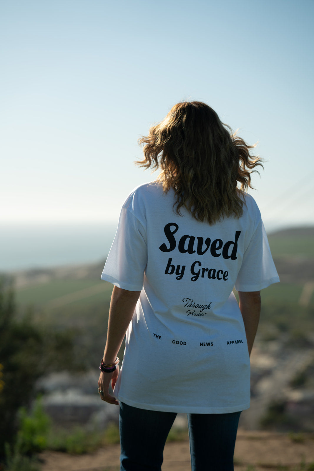 Person wearing a white t-shirt with 'Saved by Grace' text, standing outdoors.
