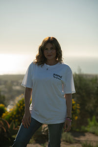 Woman wearing a white t-shirt with 'saved by grace' text, standing outdoors with a scenic background.