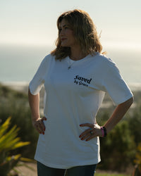 Woman wearing a white t-shirt with 'saved by grace' text outdoors.