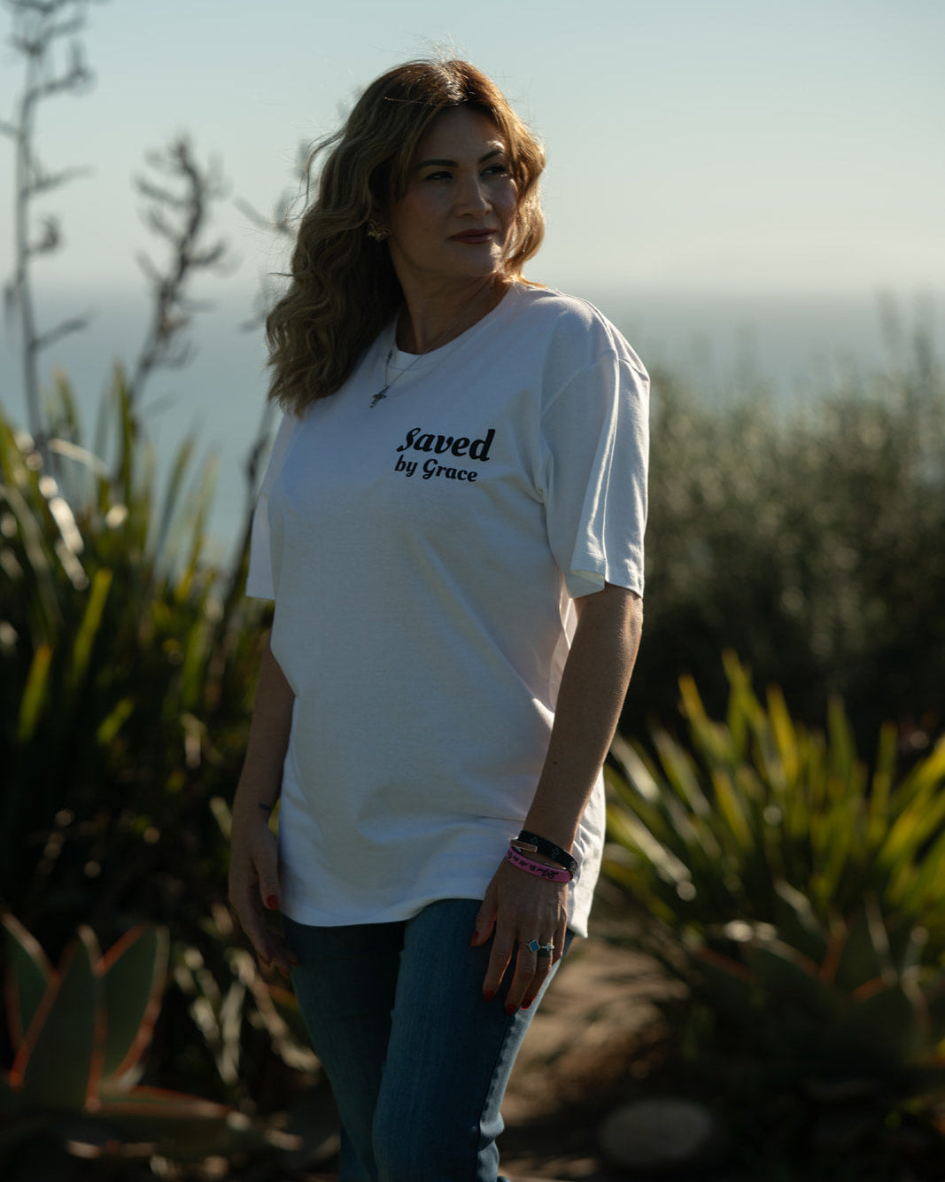 Woman wearing a white t-shirt with text standing outdoors among plants