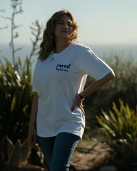 Woman wearing a white t-shirt with text standing outdoors with plants and sky in the background