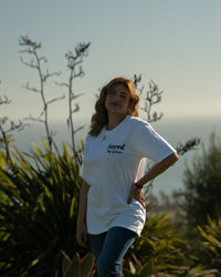Woman standing outdoors with plants and a clear sky in the background