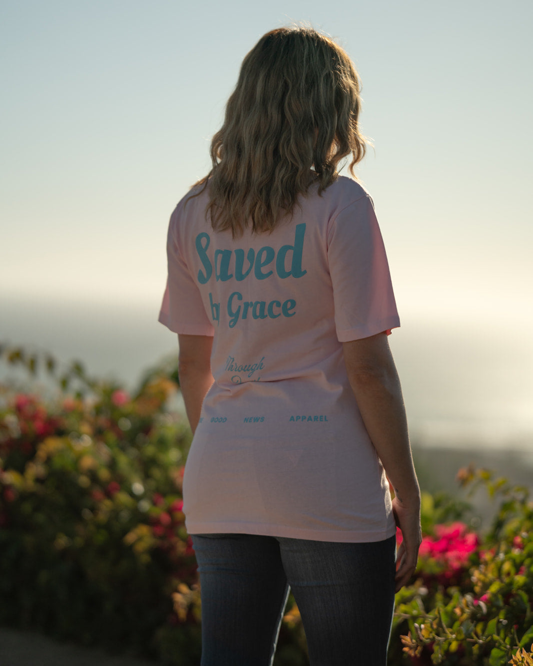 Person wearing a 'Saved by Grace' t-shirt standing in a scenic outdoor setting.