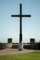 Person kneeling in front of a large wooden cross on a clear day.