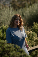 Woman wearing a blue t-shirt with text, standing outdoors among greenery