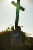 Person wearing a shirt with 'Saved by Grace' standing in front of a cross